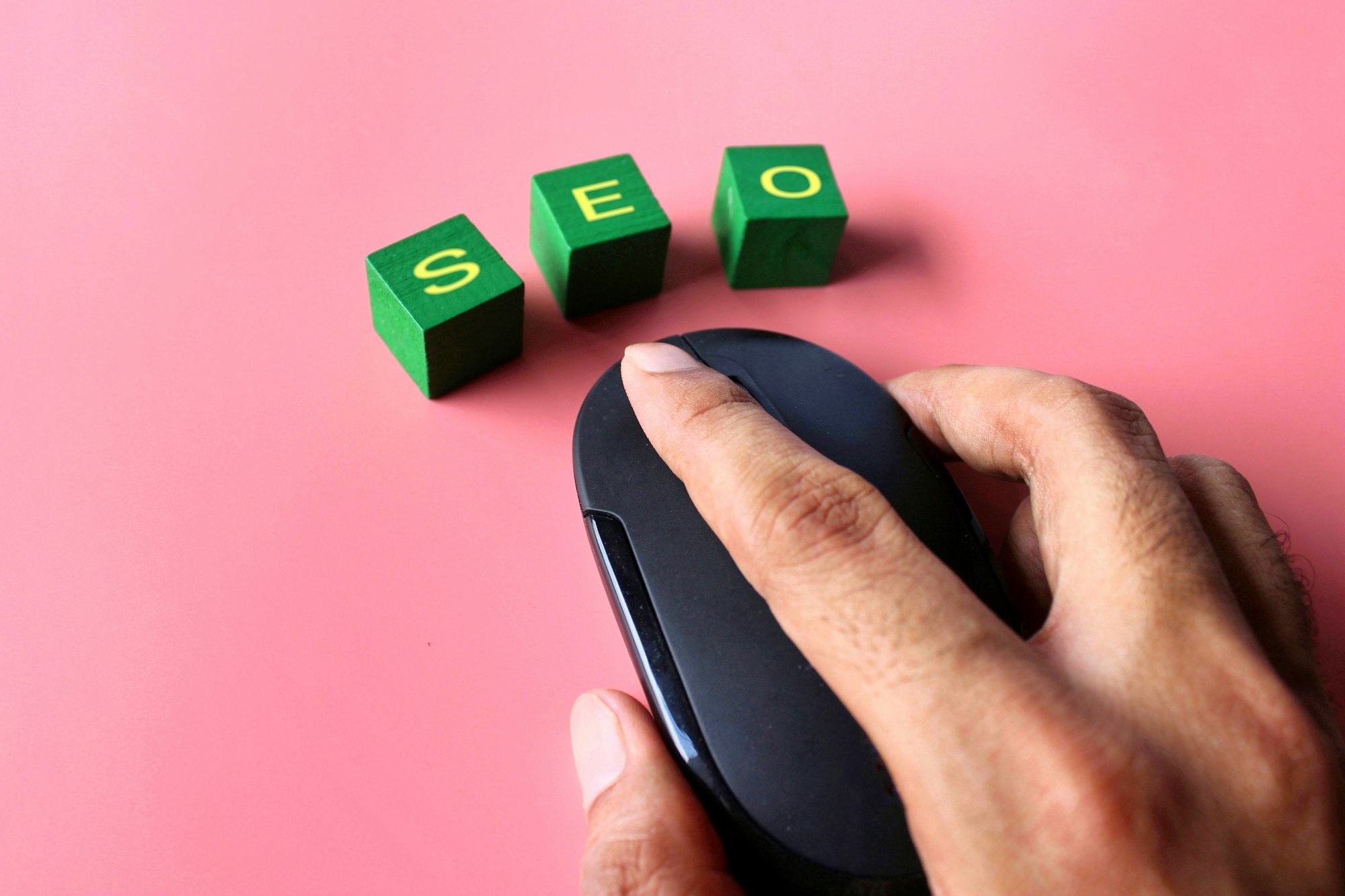 Hand click computer mouse with text SEO on pink background