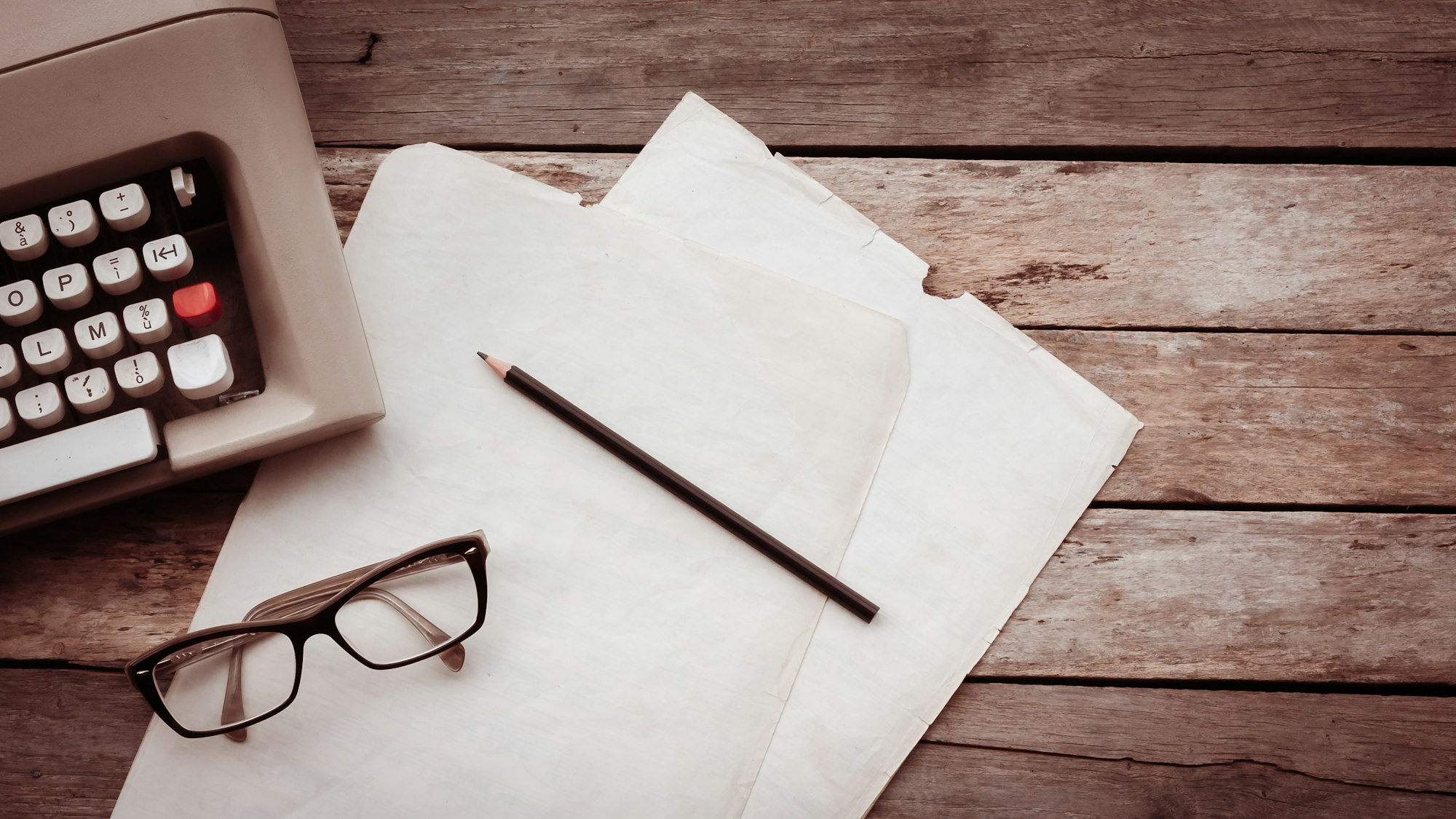 Typewriter, pensil, glasses and paper on wooden background.